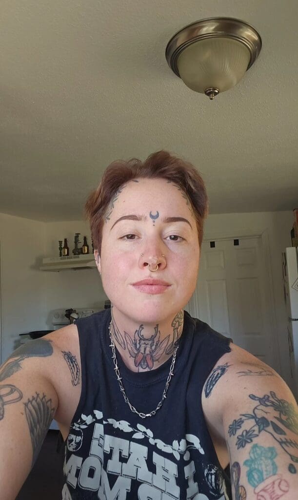 Selfie of Bridgett Barnes, a non-binary person with tattoos and wearing a tank top