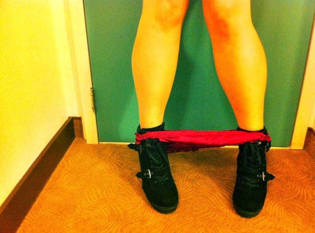 An image of bare legs wearing black shoes with her underwear down to her feet