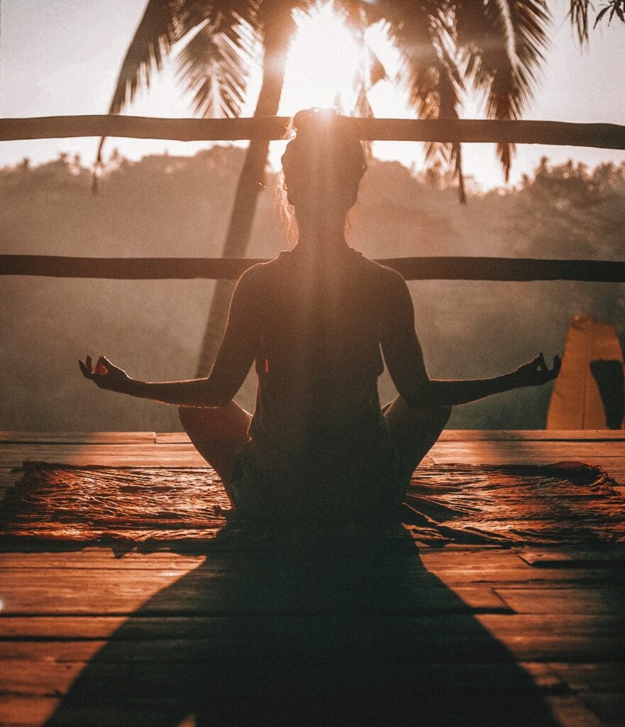 Image shows womaan meditating at sunset.